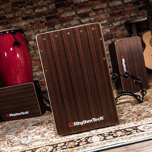 Rhythm Tech cajon in front of two other cajons, a djembe, an acoustic guitar, and a brick wall