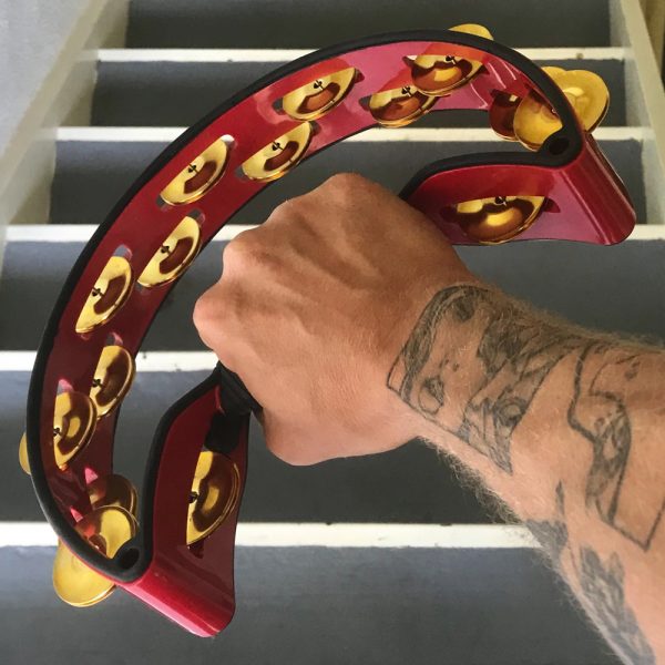 tattooed arm of man holding red Rhythm Tech crescent-shaped tambourine in front of staircase