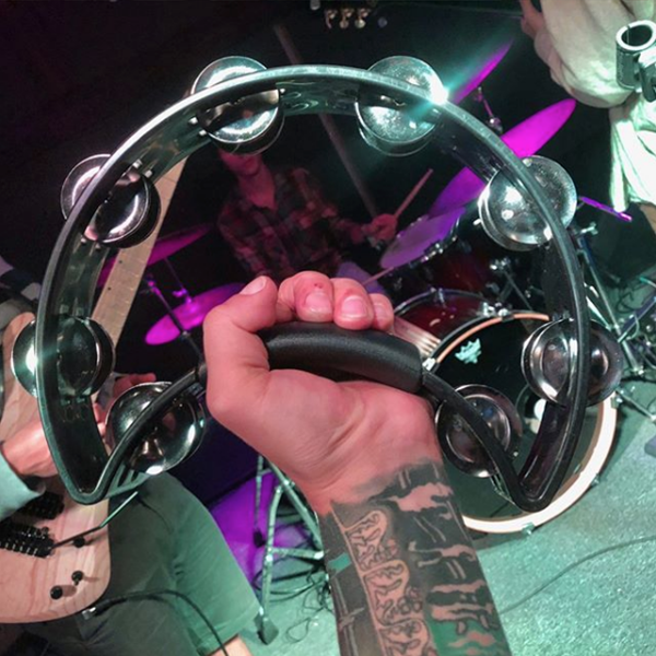 arm of man with tattoos holding black crescent-shaped tambourine