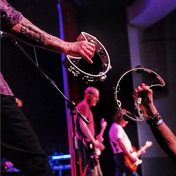 arms of two men at concert holding crescent-shaped tambourines