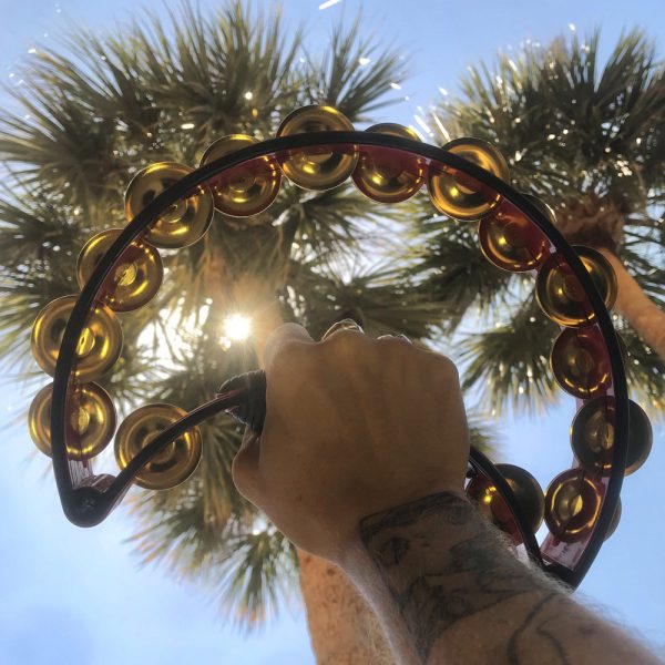 man's hand holding black Rhythm Tech tambourine up towards sky with sun and palm trees in background