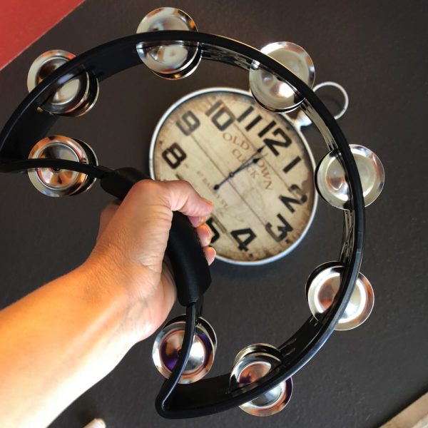 hand holding black Rhythm Tech crescent-shaped tambourine in front of clock hanging on wall