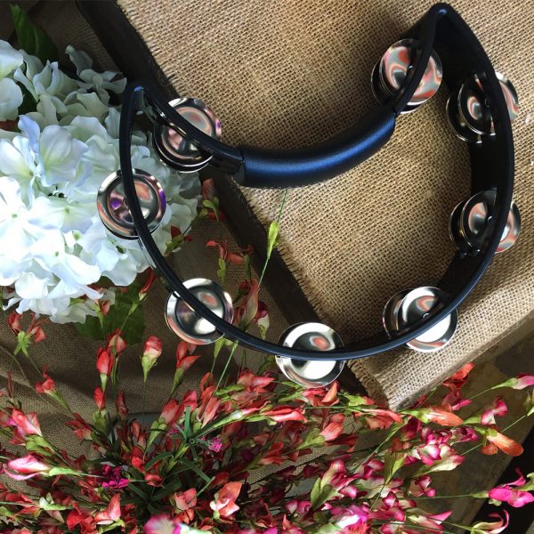 black Rhythm Tech crescent-shaped tambourine on piece of burlap material beside white and pink flowers